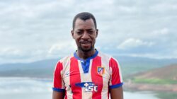 Potret seorang pria Afrika yang tersenyum dengan jersey bergaris di latar belakang pemandangan alam di Guinea.