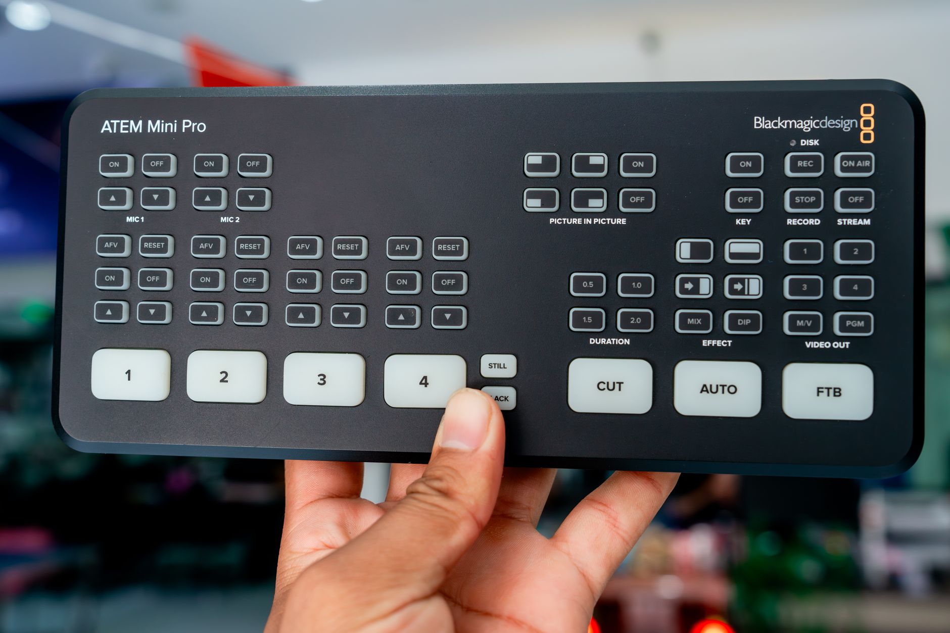 Tampilan dekat dari sebuah switcher Blackmagic Design ATEM Mini Pro yang dipegang di dalam ruangan, menampilkan tombol dan kontrolnya.