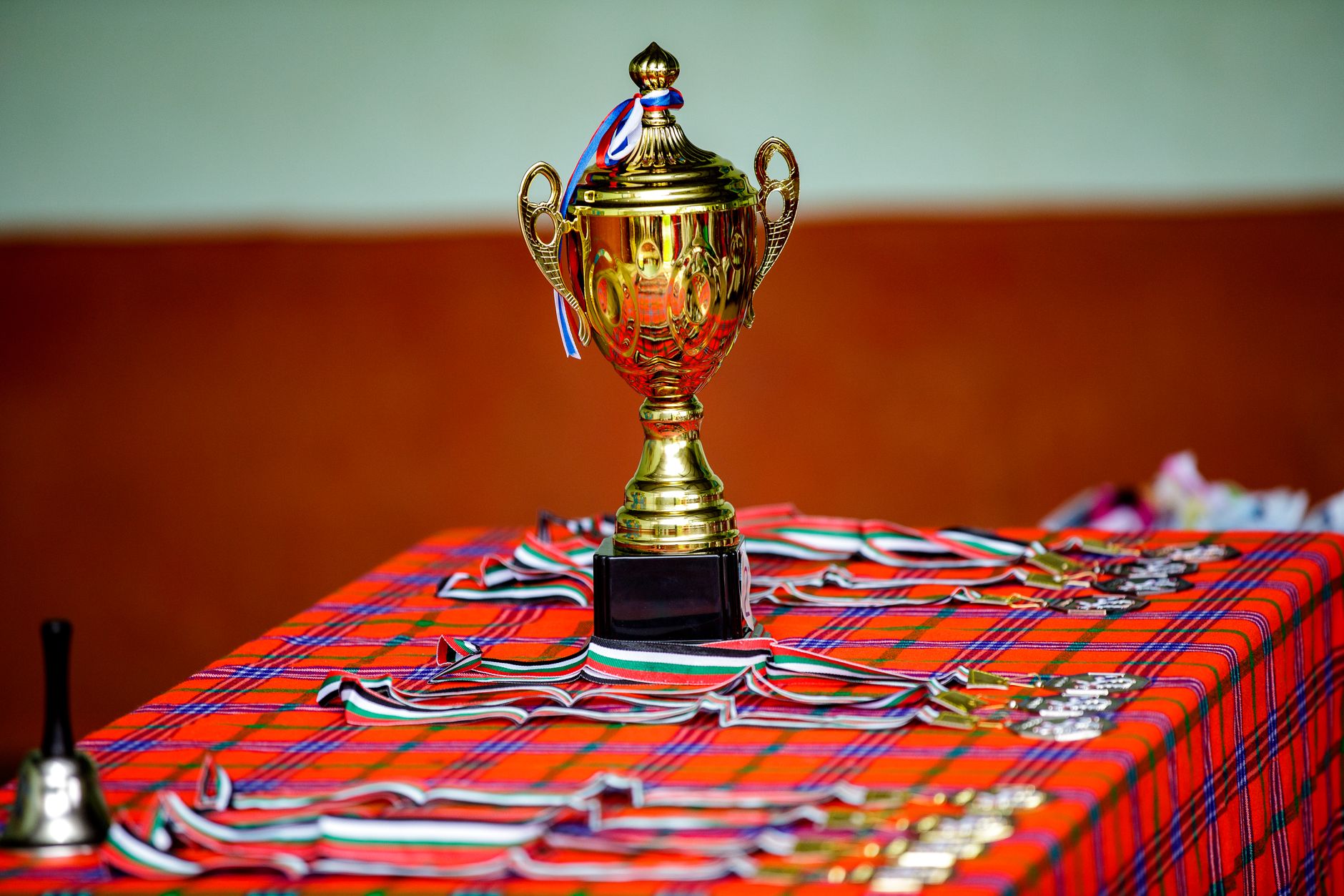 Piala emas dengan pita dan medali di atas meja kotak, melambangkan kemenangan dan pencapaian.