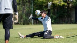 Kiper sepak bola dengan fokus tinggi saat melakukan penyelamatan selama latihan di hari yang cerah.