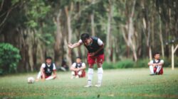 Pemain sepak bola muda berlatih di lapangan yang berdampingan, fokus pada kerja tim dan keterampilan.