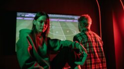 Dua orang dewasa muda bermain video game dengan intens di dalam ruangan menggunakan pengontrol game.