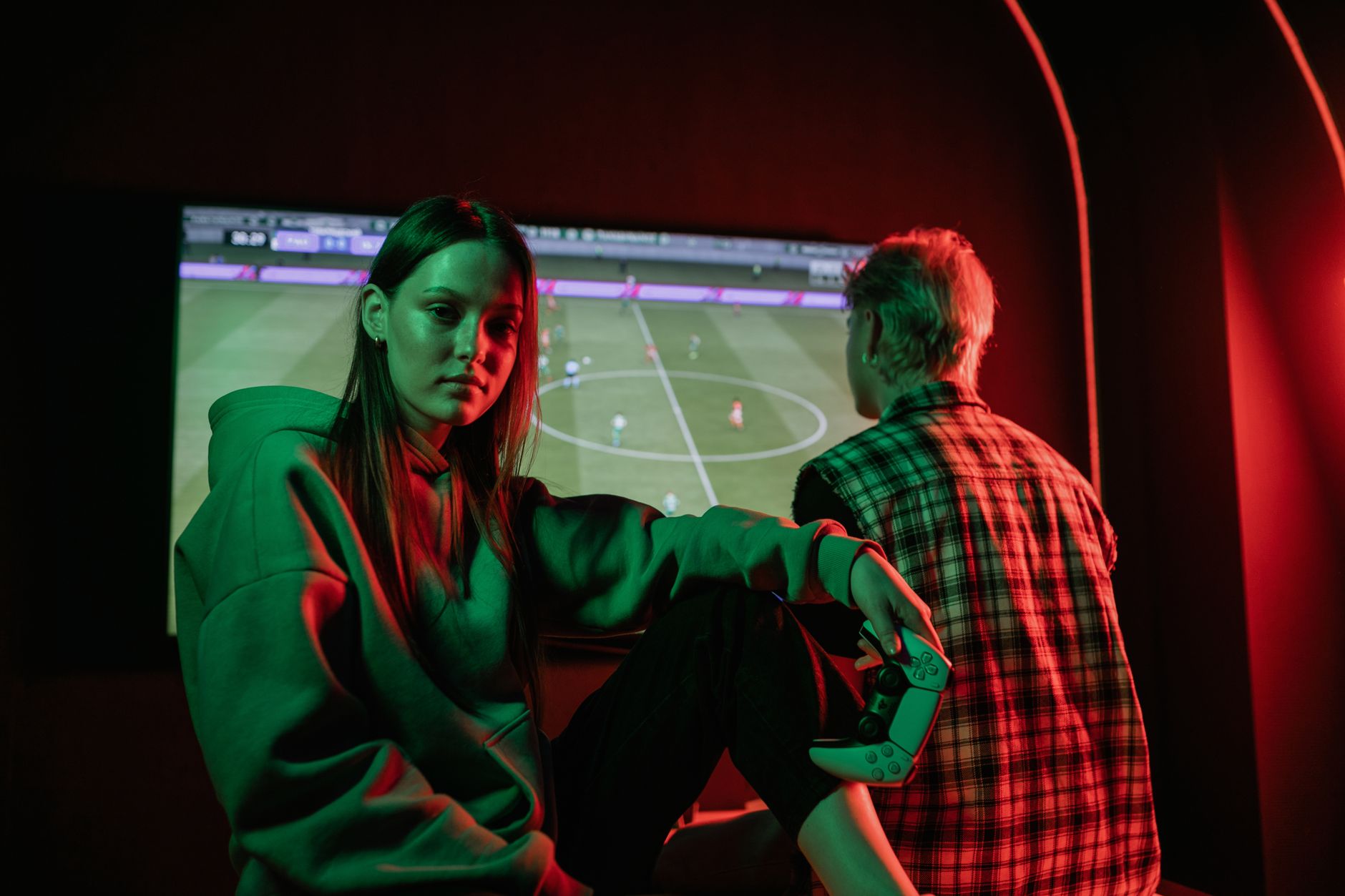 Dua orang dewasa muda bermain video game dengan intens di dalam ruangan menggunakan pengontrol game.