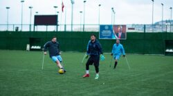 Atlet adaptif bermain sepak bola di lapangan, menunjukkan keterampilan dan tekad.
