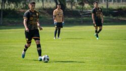 Seorang pemain sepak bola muda dalam seragam bersiap untuk mengoper pada hari yang cerah di lapangan.