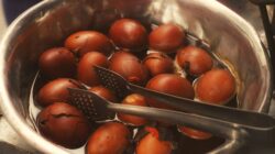 Telur rebus segar dalam rendaman teh tradisional dengan penjepit, menyoroti budaya kuliner Asia.