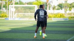 Dua pria berpartisipasi dalam sesi latihan sepak bola di luar ruangan pada hari yang cerah, berlatih keterampilan bermain bola.