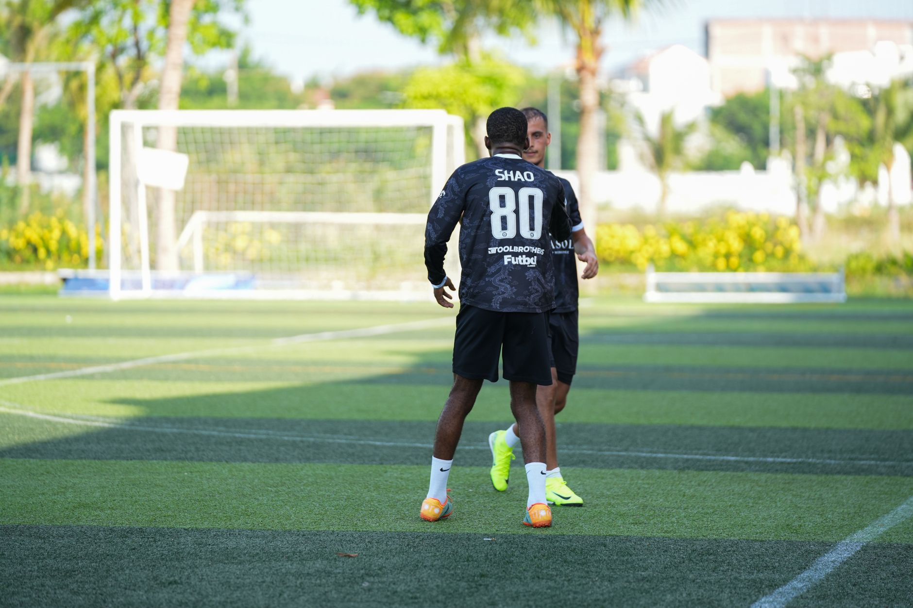 Dua pria berpartisipasi dalam sesi latihan sepak bola di luar ruangan pada hari yang cerah, berlatih keterampilan bermain bola.