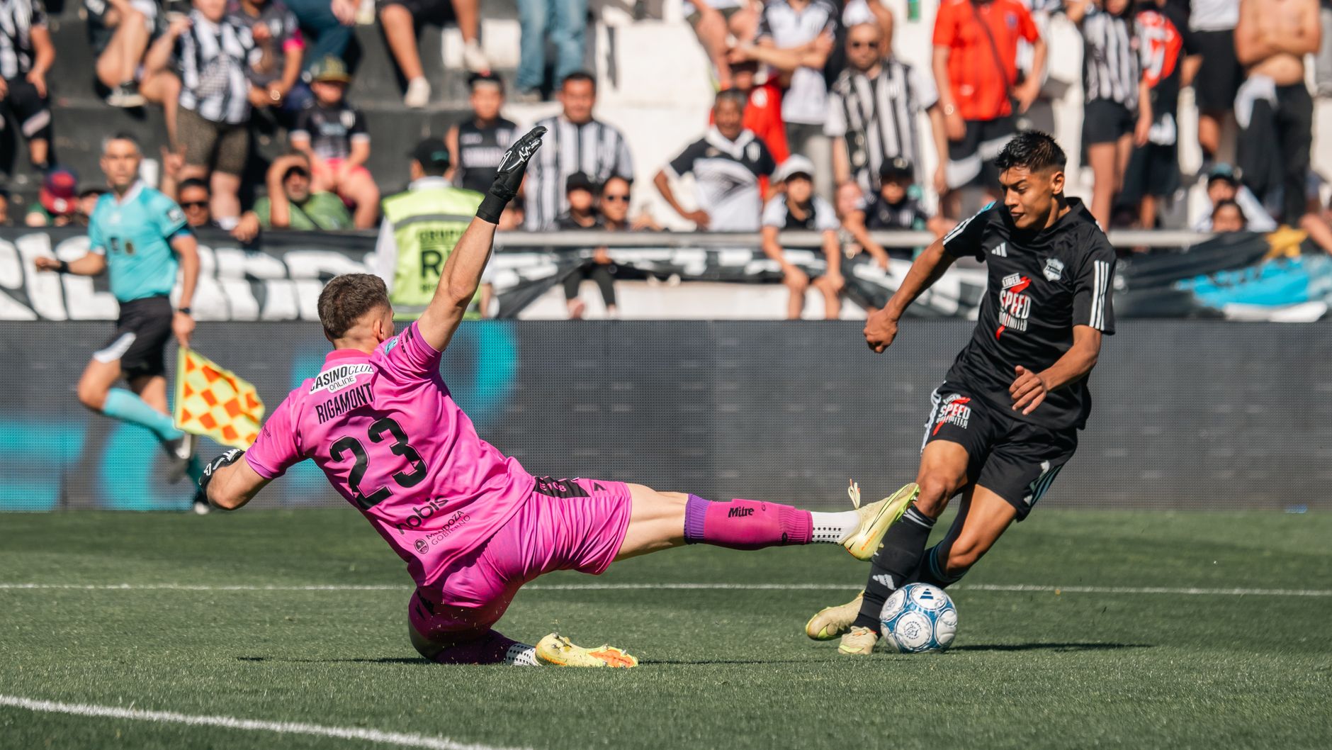 Kiper berbaju merah muda meluncur untuk menghalangi penyerang berbaju hitam selama pertandingan sepak bola.