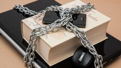 Buku terkunci dengan rantai, ponsel, dan laptop yang melambangkan keamanan digital dan intelektual.