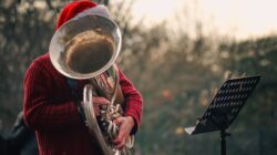 Seorang musisi mengenakan topi Santa tampil dengan tuba di luar ruangan, menciptakan suasana meriah.