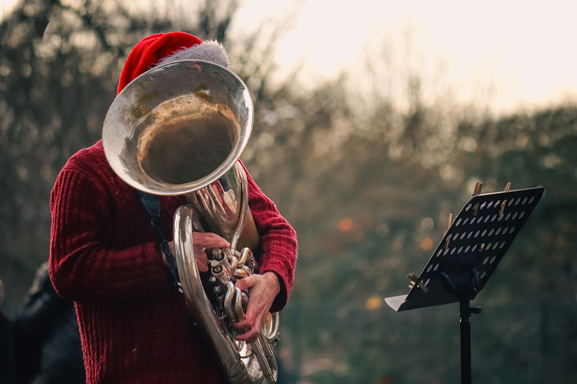 Seorang musisi mengenakan topi Santa tampil dengan tuba di luar ruangan, menciptakan suasana meriah.