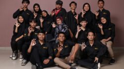 Sekelompok remaja yang beragam dan seorang wanita dewasa berpose dalam pakaian hitam, membuat tanda tangan.