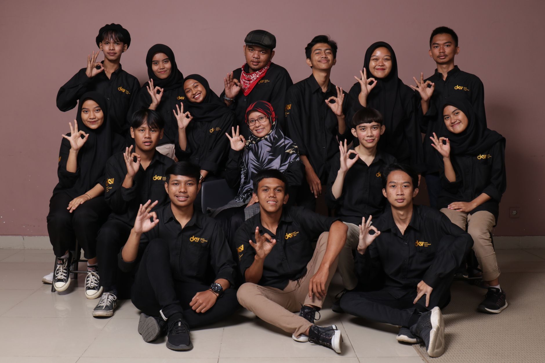 Sekelompok remaja yang beragam dan seorang wanita dewasa berpose dalam pakaian hitam, membuat tanda tangan.