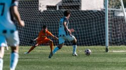 Pertandingan sepak bola yang menarik dengan upaya tembakan dekat yang diblok oleh seorang kiper yang beraksi di bawah sinar matahari.