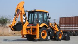 Backhoe loader ACE AX 124 pada hari yang cerah di lokasi konstruksi Faridabad.