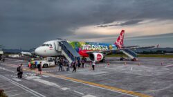 Pesawat Air Asia yang cerah dengan desain bertema Indonesia di Bandara Jogja, menangkap esensi perjalanan.