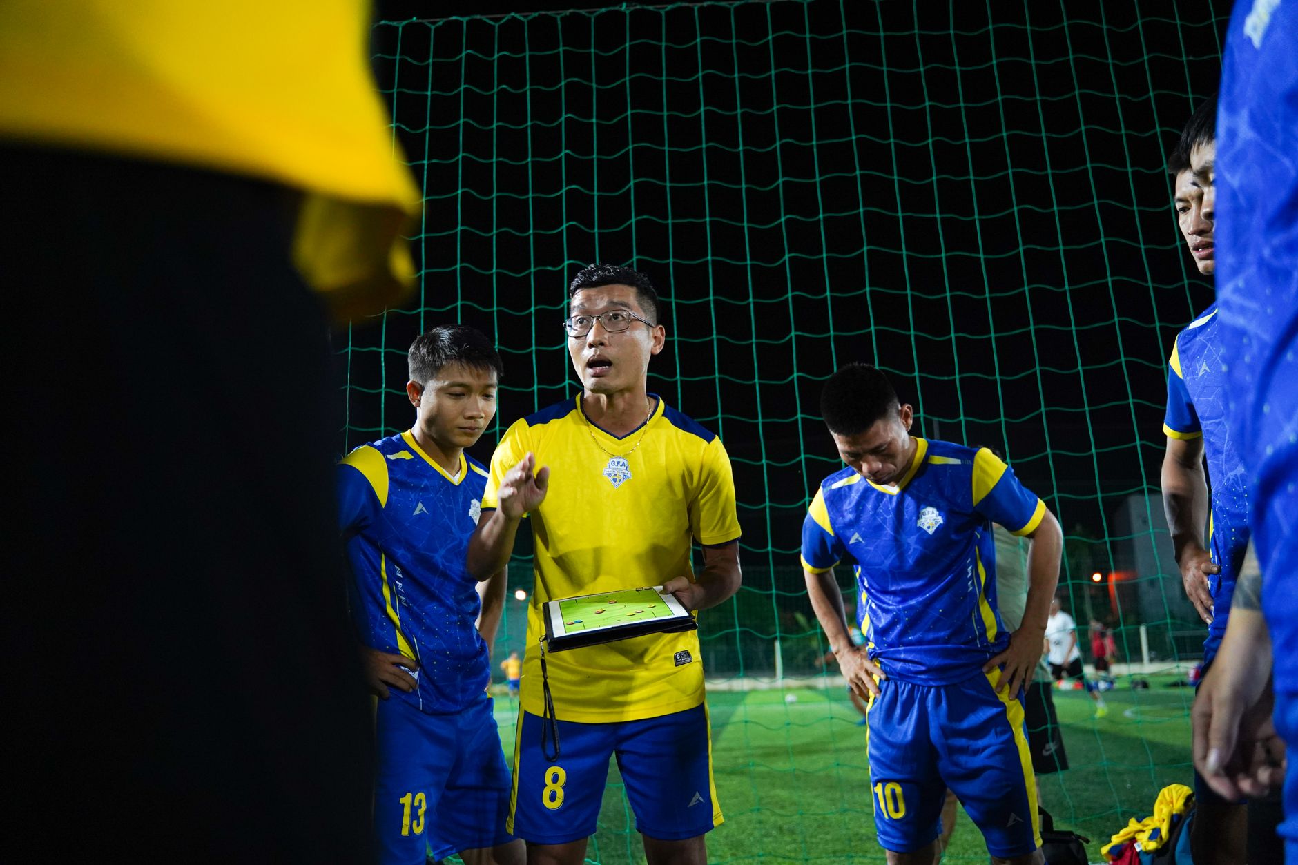 Pelatih sepak bola memberikan pembicaraan strategi kepada pemain di lapangan malam.