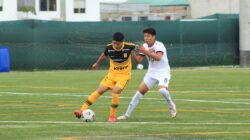 Dua pemain sepak bola remaja bersaing sengit di lapangan selama pertandingan.