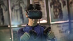 Seorang pria muda menggunakan headset VR dan pengontrol untuk pengalaman bermain yang imersif di dalam ruangan.