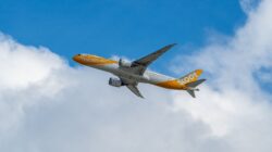 Sebuah pesawat flyscoot terbang menembus langit biru cerah dengan awan halus.