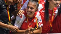 Pemain sepak bola wanita yang tersenyum merayakan dengan medali setelah kemenangan. Momenn tim di luar ruangan yang cerah.