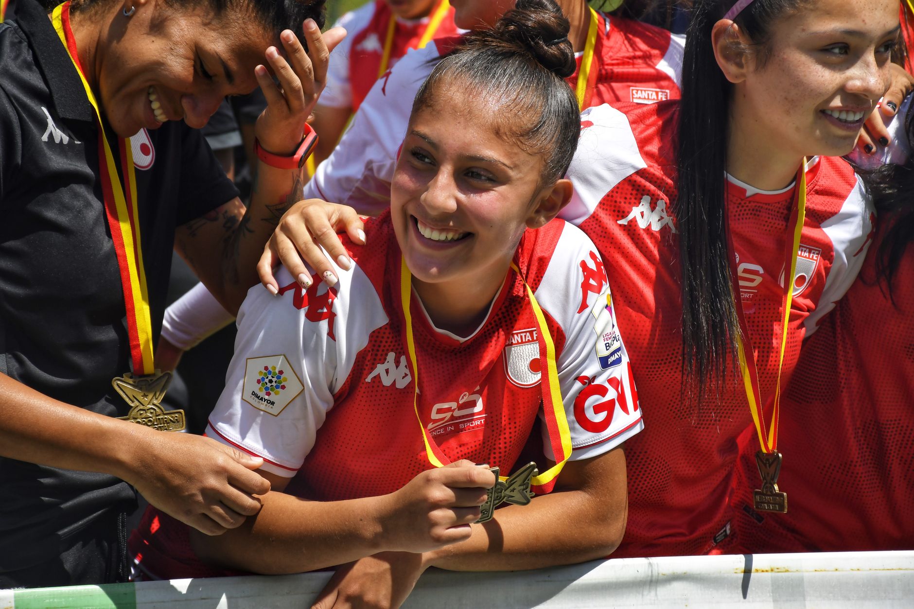 Pemain sepak bola wanita yang tersenyum merayakan dengan medali setelah kemenangan. Momenn tim di luar ruangan yang cerah.