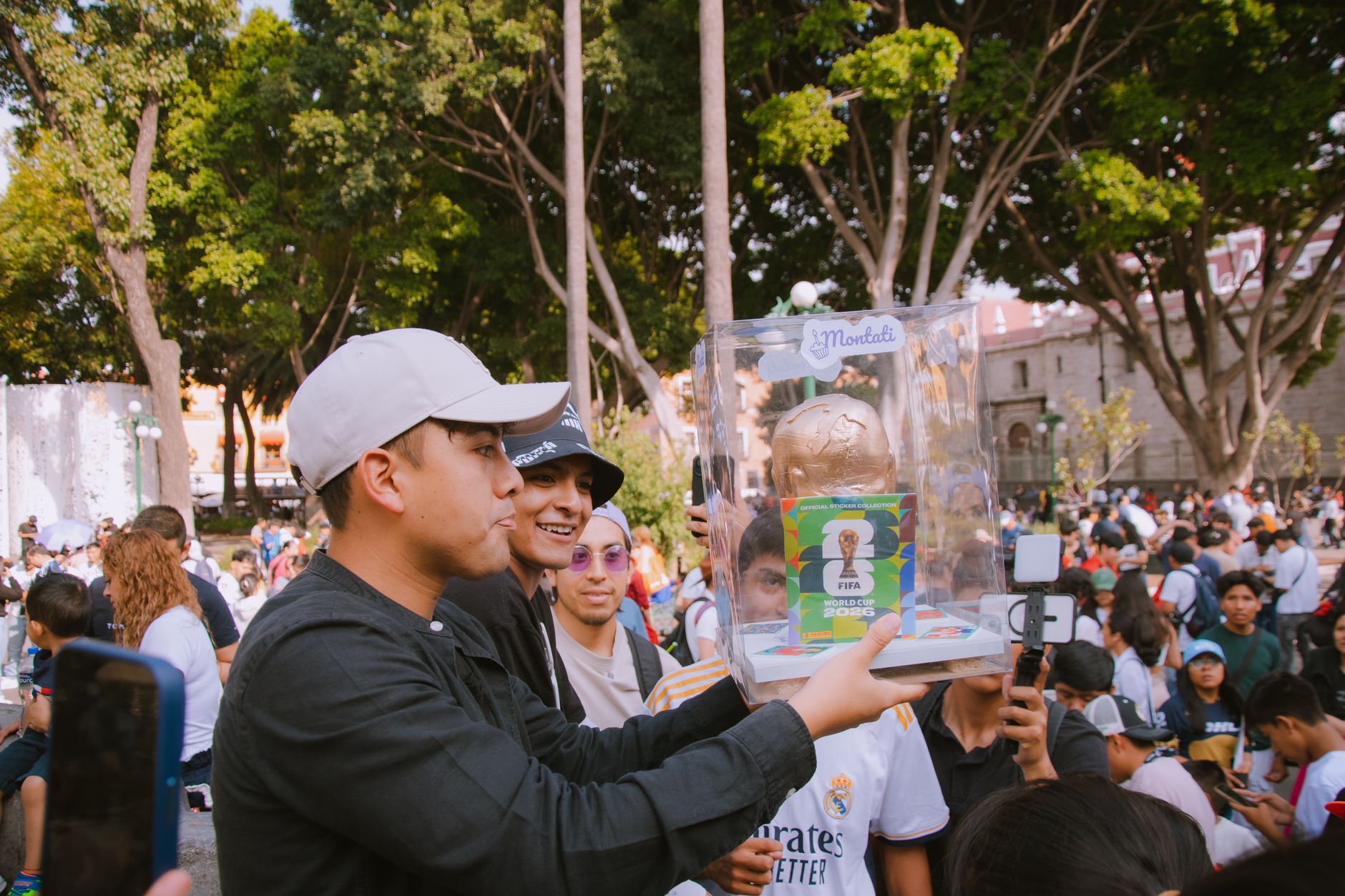 Sekelompok orang merayakan dengan replika trofi FIFA Piala Dunia di lingkungan luar ruangan yang semarak.