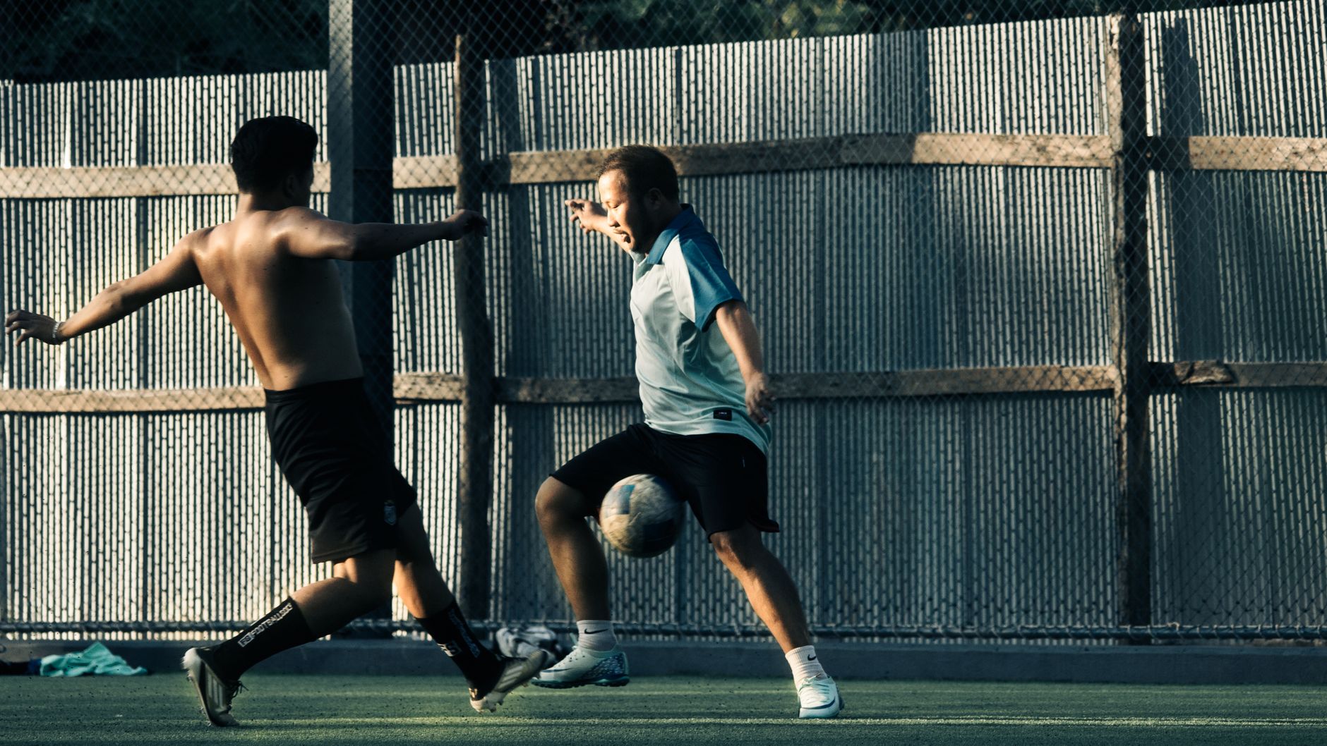 Dua pria terlibat dalam pertandingan sepak bola yang intens, menampilkan aksi dan ketangkasan di luar ruangan.
