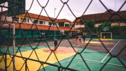 Orang-orang bermain di lapangan basket luar ruangan yang dikelilingi oleh pagar jaring.