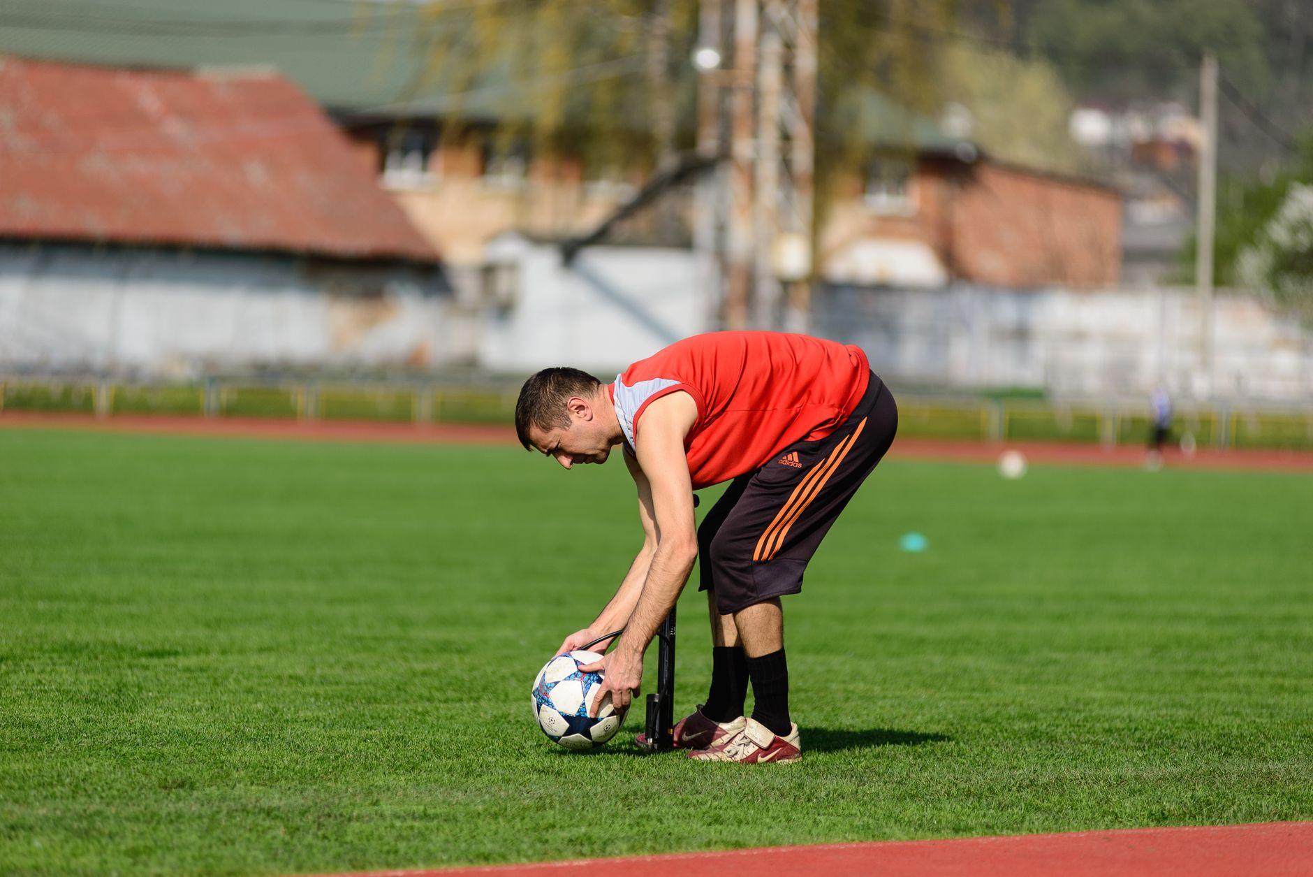 Seorang atlet dalam pakaian olahraga sedang menyiapkan bola sepak di lapangan rumput saat pelatihan siang hari.
