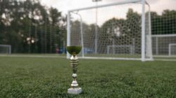 Trofi emas yang ditempatkan di rumput hijau dekat gawang sepak bola, melambangkan kemenangan.