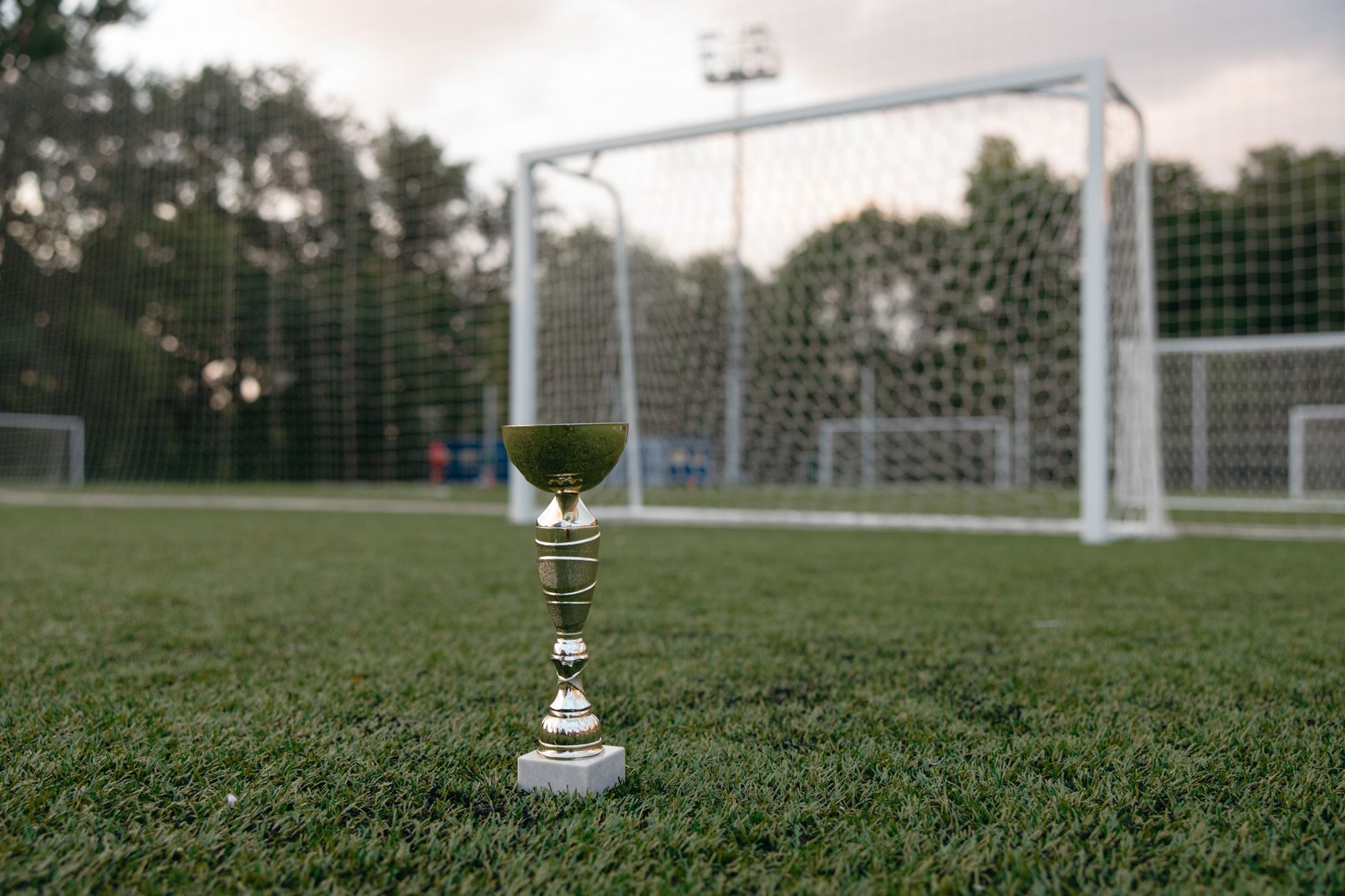 Trofi emas yang ditempatkan di rumput hijau dekat gawang sepak bola, melambangkan kemenangan.