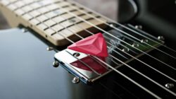 Gambar detail dari pilih gitar merah yang terletak di senar gitar listrik.