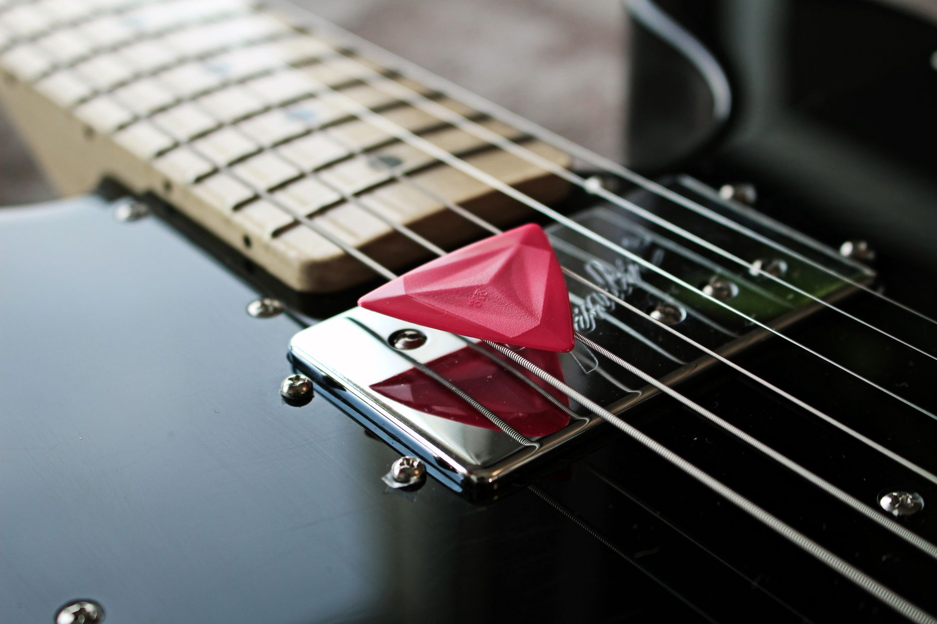 Gambar detail dari pilih gitar merah yang terletak di senar gitar listrik.