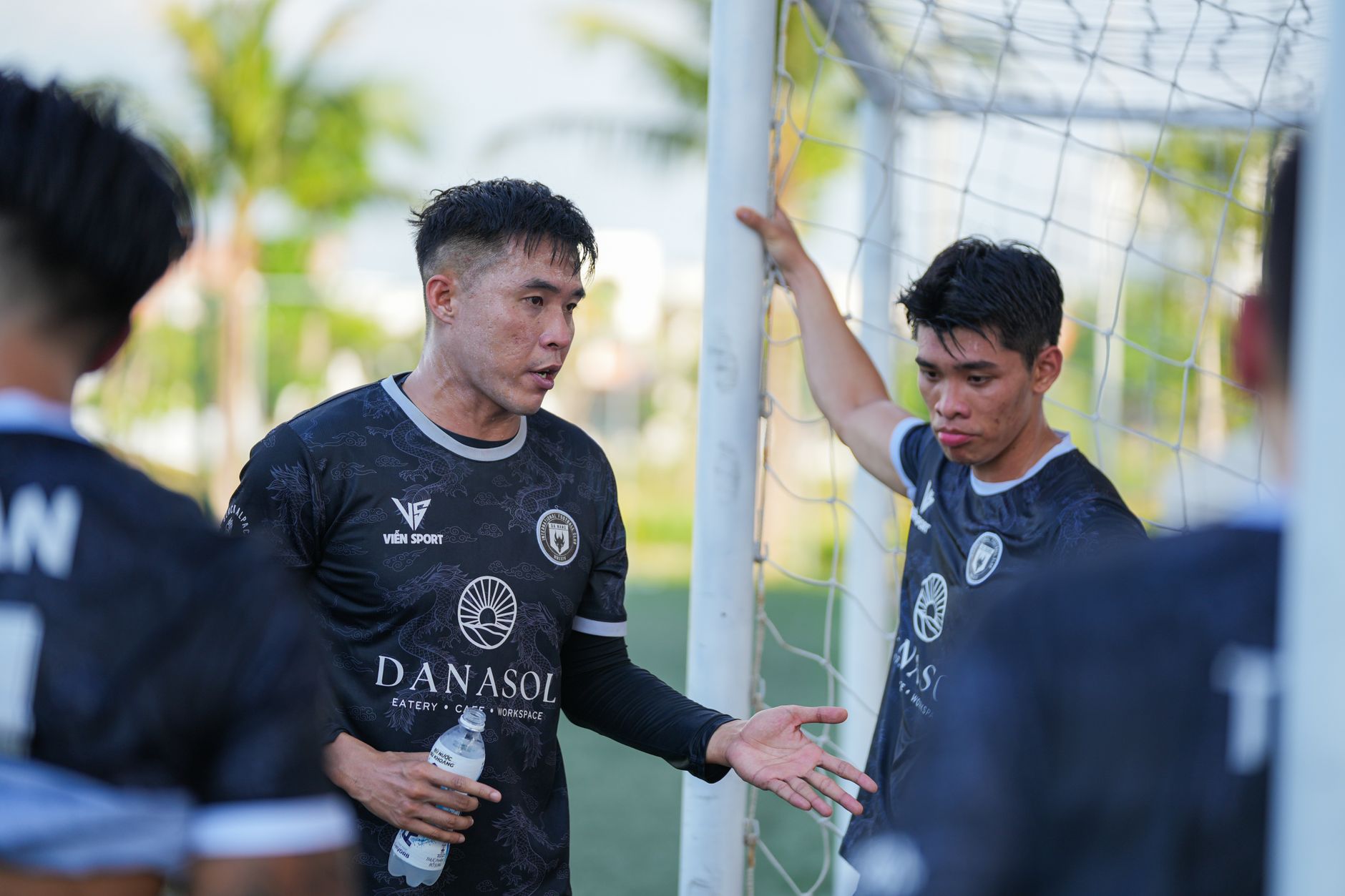 Dua pemain sepak bola mendiskusikan strategi di lapangan dekat tiang gawang di luar ruangan.